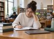 Persona joven estudiando en una biblioteca con cuaderno, libros y ordenador cerrado