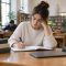 Persona joven estudiando en una biblioteca con cuaderno, libros y ordenador cerrado