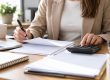 Manos de una trabajadora con bolígrafo y calculadora ante varias hojas blancas