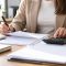 Manos de una trabajadora con bolígrafo y calculadora ante varias hojas blancas